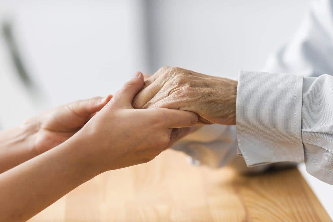 A carer reassuringly holding an older person's hands